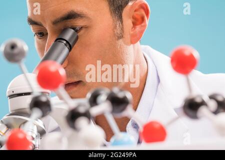 Close-up of scientist looking through microscope, molecular model in foreground Stock Photo