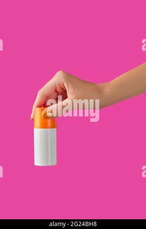 Manicured womans hand holding sunscreen bottle on pink background Stock Photo