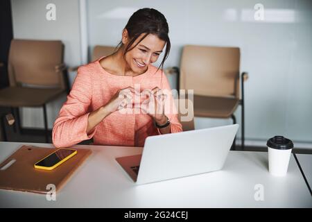 Smiling pretty online teacher talking with participants on video call while using laptop Stock Photo