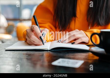 Brunette woman writing down notes while sitting in cafe Stock Photo