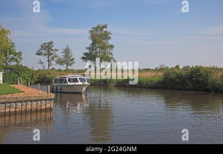 A small cruiser on the River Ant on the Norfolk Broads passing by Irstead Staithe at Irstead, Norfolk, England, United Kingdom. Stock Photo