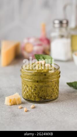 Pesto sauce in a glass jar with basil leaves and a slice of parmesan cheese. Italian cuisine. Stock Photo