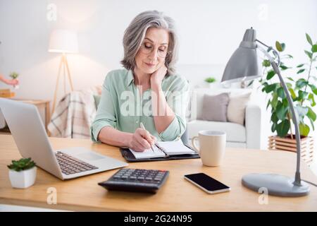 Photo of pretty serious woman arm hole pen take notes notepad sit behind desk working from home indoors Stock Photo