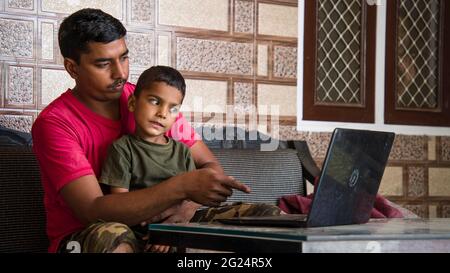 Man and cute child using laptop. Working Indian father works from home office with kid in pandemic. Stock Photo