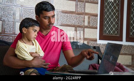 Indian father teaching adorable little daughter to use laptop. Online study concept. Stock Photo