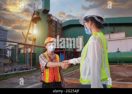 Two engineers shaking hands in front of a factory, Thailand Stock Photo