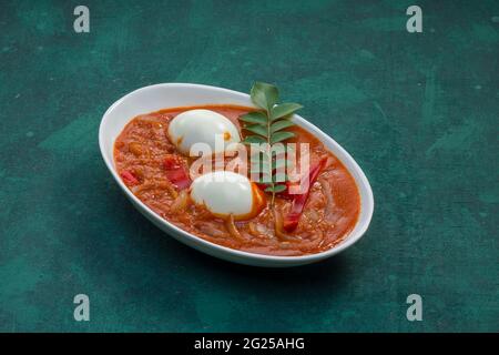 Egg roast or Indian egg masala curry,spicy red egg roast arranged in a white ceramic bowl with dark green  texture Stock Photo