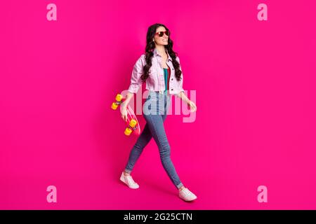 Full size profile side photo of young beautiful cool confident girl go walk with skateboard isolated on pink color background Stock Photo