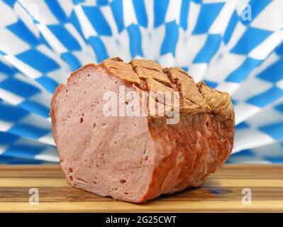 warm bavarian meat loaf or leberkaese on a wooden plate served in front of a typical bavarian diamand pattern Stock Photo