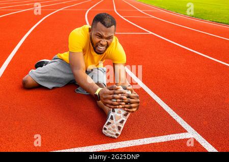 Young focused attractive African American athlete sportsman stretching on racetrack at city stadium. Serious African American sportsman work hard Stock Photo