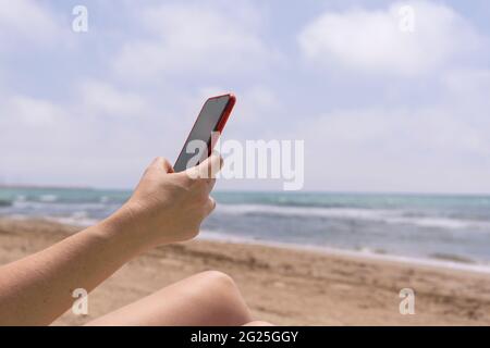 Unrecognizable woman using smart phone on the beach.Hand holding cellphone on summer holidays background. Stock Photo