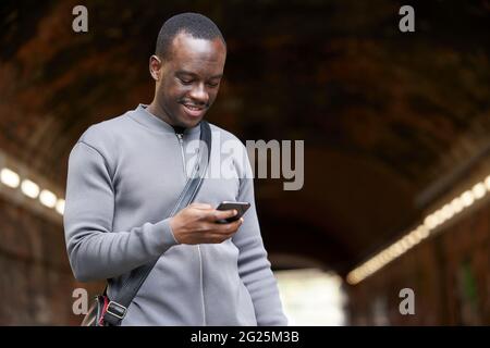 Smiling Young Man In Urban Setting Checks Messages And Social Media On Mobile Phone Stock Photo