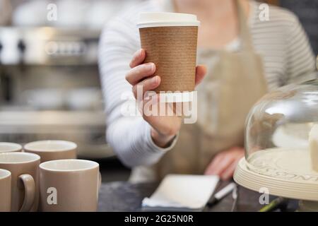 Close Up Of Female Worker in Cafe Serving Coffee In Sustainable Paper Cup Stock Photo