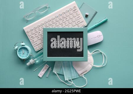 Presenteeism term written on blackboard. Flat lay in monochrome mint blue hues. Office supplies, keyboard, mouse, alarm clock, pens, reading glasses Stock Photo