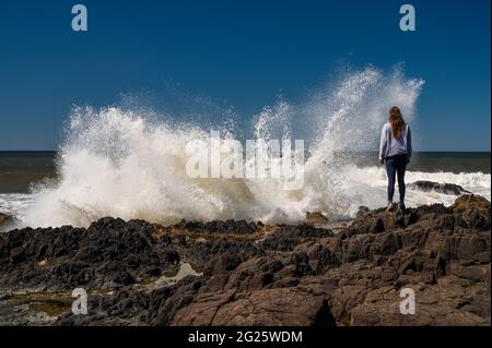 Female Standing On The Coast With Waves Crashing Stock Photo