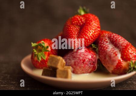 Red ripe strawberries on round plate with a few cane sugar pieces and melted white chocolate Stock Photo