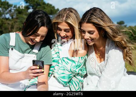 Three female friends using mobile phone and having fun Stock Photo