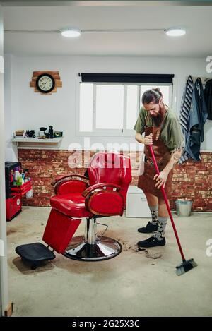 A barber cleaning the hairs on the floor of his barbershop. Stock Photo