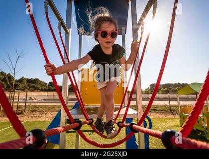 Young girl on climbing frame at outdoor park in sunshine Stock Photo