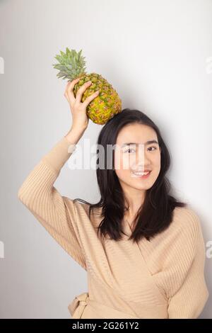 Young Asian Woman holding a pineapple on her head Stock Photo