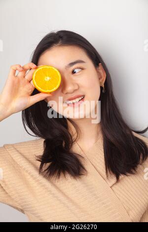 Young Asian Woman holding a orange cut in half in front of her eye Stock Photo