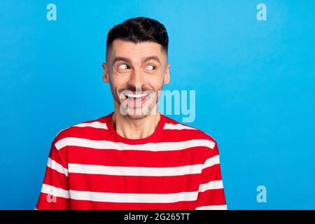 Photo of tricky funny young guy dressed red t-shirt looking empty space isolated blue color background Stock Photo