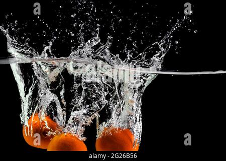 three tangerines fall into the water on a black background, copy space Stock Photo