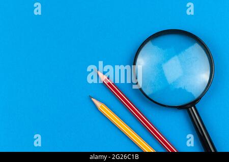 School supplies flat lay background, pencils and magnifying glass on blue office desk, top view, copy space Stock Photo