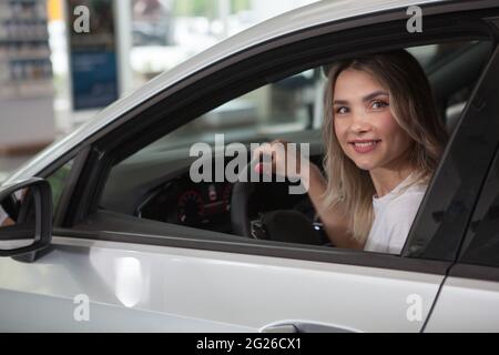 Charming young woman smiling to the camera, sitting inside new automobile at dealership Stock Photo