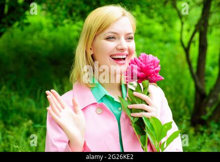 Smiling blonde woman with peony flower outdoors. Beautiful girl in garden. Stock Photo