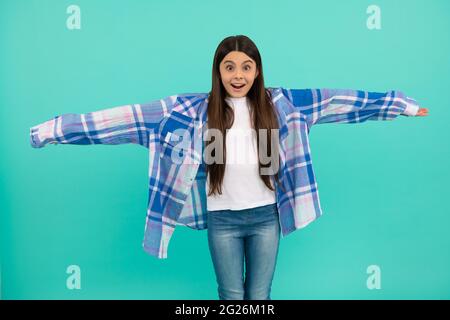 Surprised kid try on oversized plaid shirt with extra long sleeves blue background, fashion Stock Photo