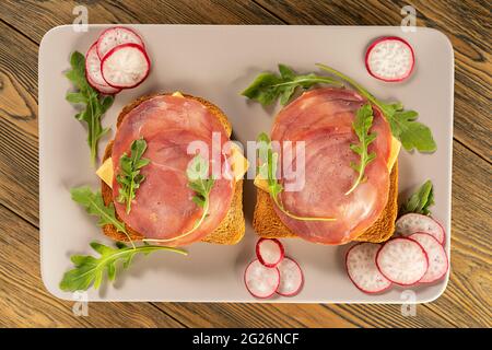 Breakfast. Sandwich with cheese and smoked sausage. Toasted horseradish. Arugula grass. Top view, rustic style. Fresh radish. Stock Photo