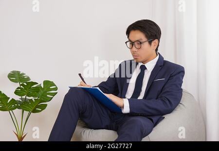 Asian Financial Advisor Wear Glasses Write Statement in Home Office.Businessman Work at Home for Social Distance or Home Quarantine in Covid 19 Stock Photo