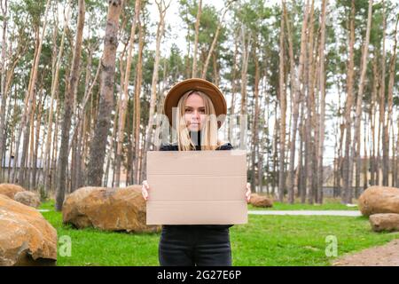 Portrait of caucasian young woman standing with cardboard outdoors. Nature background. Copy space for text Sustainable lifestyle Stock Photo