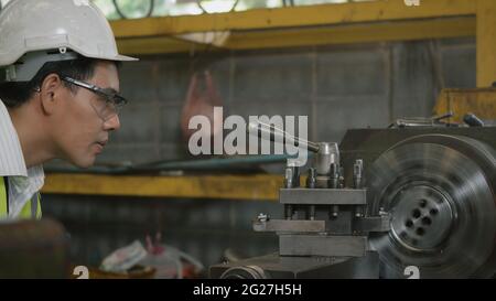 Asian professional mechanical engineer or operation man wear uniform goggles safety working on workshop metal lathe industrial manufacturing factory, Stock Photo