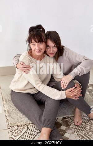 High angle of happy young woman and middle aged mother in comfy casual outfits embracing and looking at camera Stock Photo