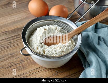 bowl and flour in strainer on kitchen table for making dough Stock Photo