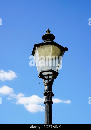 Old black metal street lamp. Blue sky with clouds in the background. Stock Photo