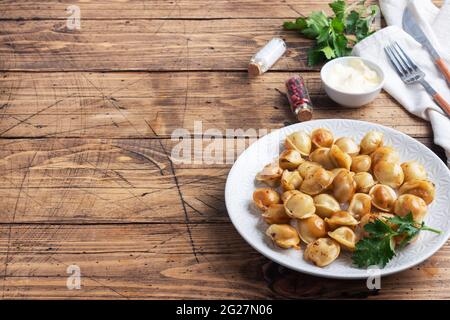 Traditional fried pelmeni, ravioli, dumplings filled with meat on plate, russian kitchen. Wooden rustic table, copy space Stock Photo