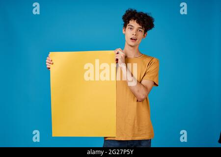 guy with curly hair yellow posters in hands Copy Space blue background studio Stock Photo