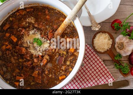 Traditional italian stew with lentils, panchetta,  vegetables and parmesan cheese served on rustic and wooden table background.  Top view Stock Photo