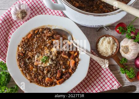 Traditional italian stew with lentils, panchetta,  vegetables and parmesan cheese served on rustic and wooden table background.  Top view Stock Photo