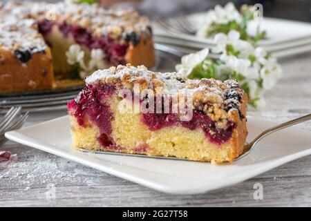 A piece of rustic cherry cake with crumbles served on a plate. Closeup view with whole cake in the background. Stock Photo