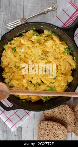 Scrambled eggs in a cast iron pan with rye bread. Closeup and top view with rustic background Stock Photo