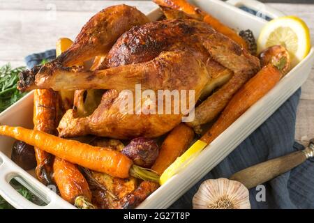 Roast chicken with oven vegetables served in a baking dish on rustic and wooden table background. Closeup and isolated view Stock Photo