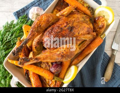 Roast chicken with oven vegetables served in a baking dish on rustic and wooden table background. Closeup and isolated view