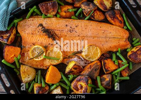 Mediterranean fish meal with vegetables and sweet potatoes served on a baking sheet from above. Closeup and isolated view. Stock Photo
