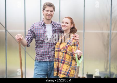 Smiling woman and man in plaid shirts in greenhouse Stock Photo