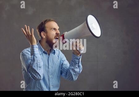 Excited young businessman in a blue shirt holding a megaphone and shouting like crazy Stock Photo