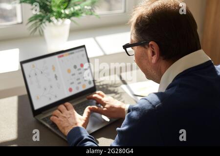 Senior office worker preparing infographics for a business presentation on a laptop Stock Photo